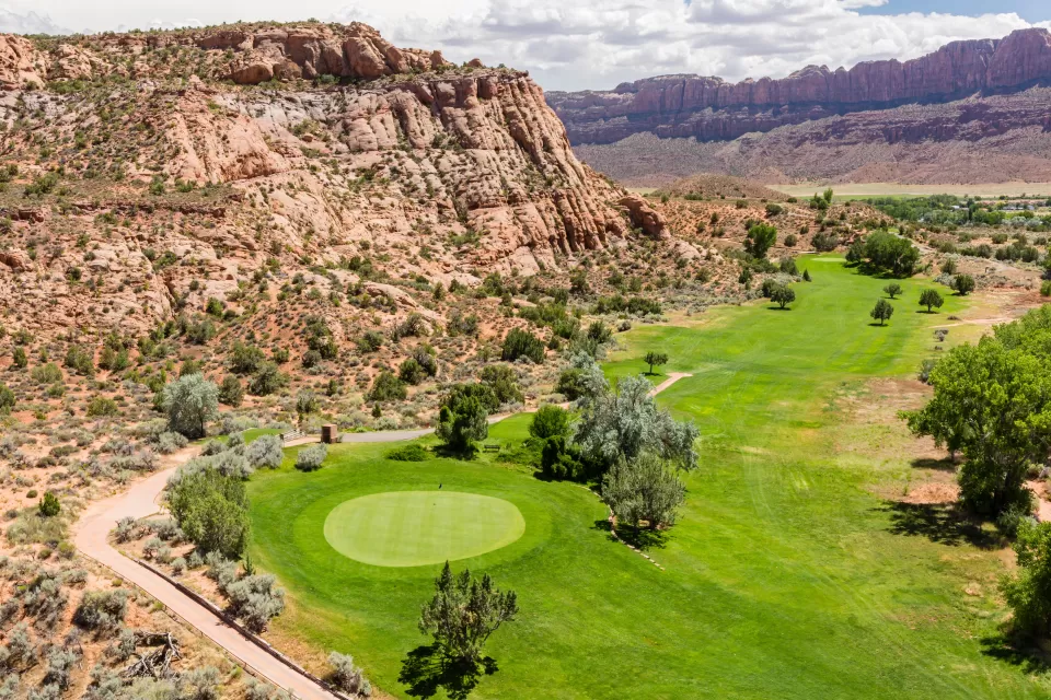 Aerial view of green colf course next to rocky desert cliffs in Moab, Utah